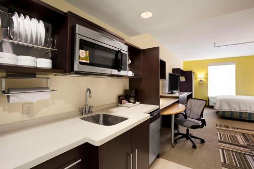 a kitchen with a sink and a room with a bed at Home2 Suites by Hilton Greensboro Airport, NC in Greensboro
