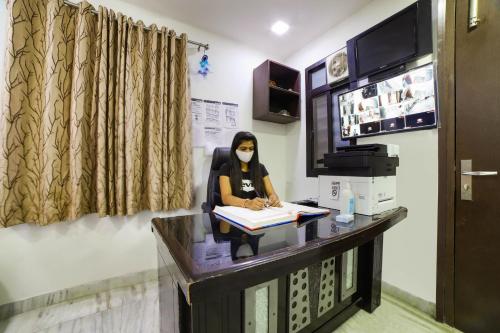 uma mulher com uma máscara sentada numa secretária em Hotel Seven S em Nova Deli
