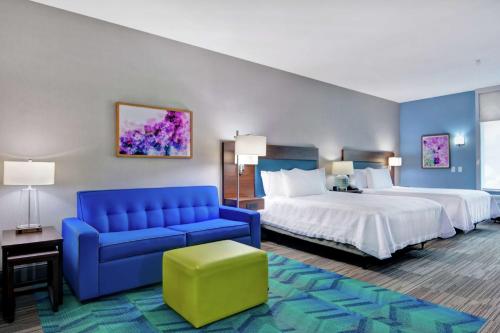 a hotel room with two beds and a blue couch at Home2 Suites By Hilton Springdale in Springdale