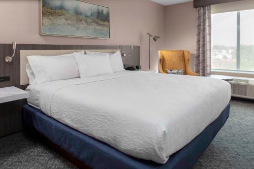 Cette chambre comprend un grand lit et une chaise. dans l'établissement Hilton Garden Inn By Hilton Fort Wayne North, à Sunnybrook Acres