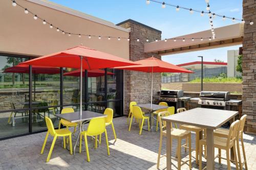 a patio with tables and yellow chairs and red umbrellas at Home2 Suites by Hilton New Brunswick, NJ in New Brunswick