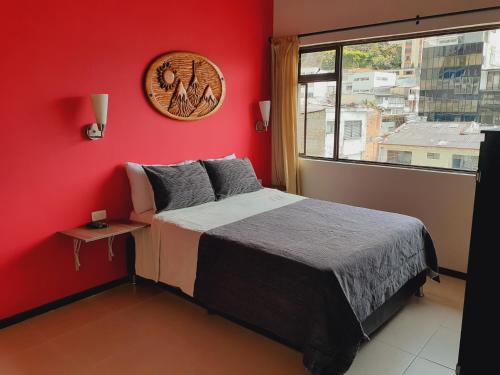 a bedroom with a red wall with a bed and a window at Ayenda Mountain Hostels Manizales in Manizales