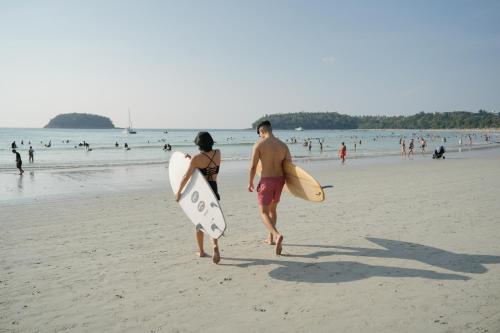 a man and woman walking on the beach with surfboards at Nonnee Hotel Kata Beach Phuket in Kata Beach