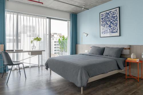a blue bedroom with a bed and a desk and a window at M Village Living Kỳ Đồng in Ho Chi Minh City