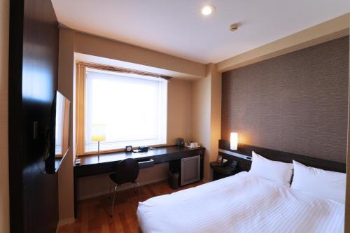 a bedroom with a bed and a desk and a window at KOKO HOTEL Sendai Kotodai Park in Sendai