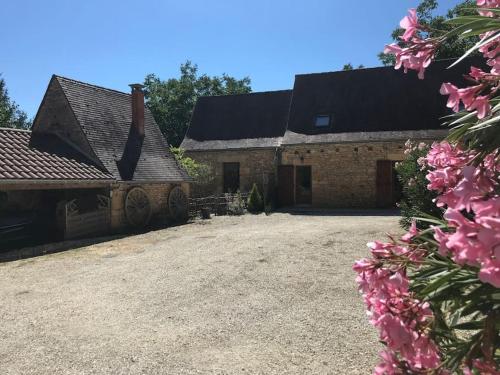 uma velha casa de tijolos com flores cor-de-rosa no primeiro plano em Grange restaurée à la campagne em Tamniès