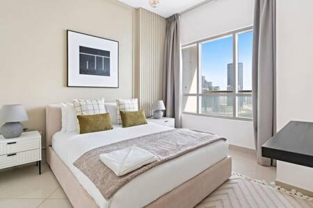 a white bedroom with a bed and a large window at Silkhaus modern 2BDR with pool and gym near Reem Central Park in Abu Dhabi