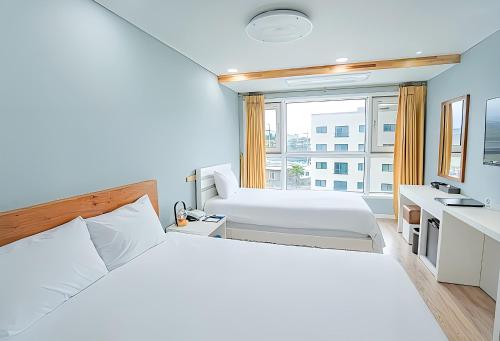 a white bedroom with two beds and a window at Hotel Sweet Castle Jeju Hamdeok in Jeju