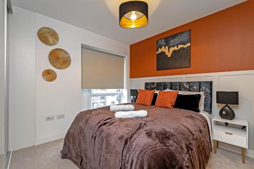 a bedroom with a large bed with an orange wall at SUPERIOR AIRPORT SUITE, FREE Parking, Stylish, BALCONY, Two Bathrooms, Close To Airport, Station & Centre in Luton