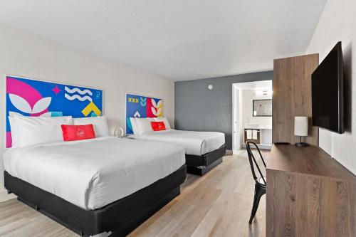a hotel room with two beds and a flat screen tv at Developer Inn Highway, A Howard Johnson by Wyndham in Kissimmee