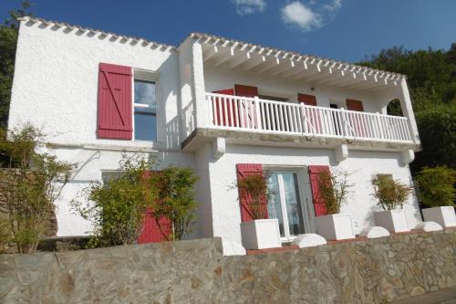 een wit huis met rode deuren en een balkon bij O Petit Bonheur in Laroque-des-Albères