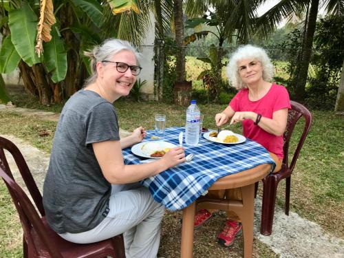 dwie starsze kobiety siedzące przy stole jedzące jedzenie w obiekcie Lucky's Homestay w mieście Maho