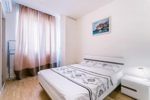 a white bedroom with a bed and a window at Stylish spacious apartment near the sea in Budva