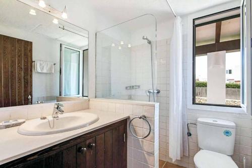 Un baño con lavabo, inodoro y espejo. en Villa Bini Blanca, en Binibeca