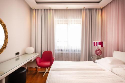 a hotel room with two beds and a red chair at Hotel Aurora in Merano