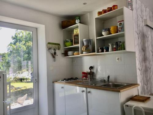 Cottage chaleureux face à l'étang في Précy: مطبخ بخزائن بيضاء ومغسلة ونافذة