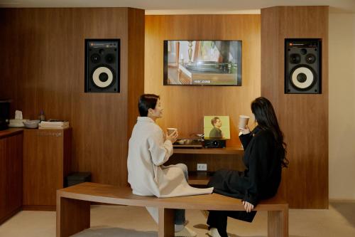 a man and woman sitting on a bench in a room with speakers at Aank Hotel Suwon in Suwon