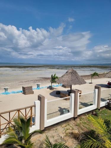a beach with a white fence and an umbrella at Kwa Mama Village Beach Resort in Dar es Salaam