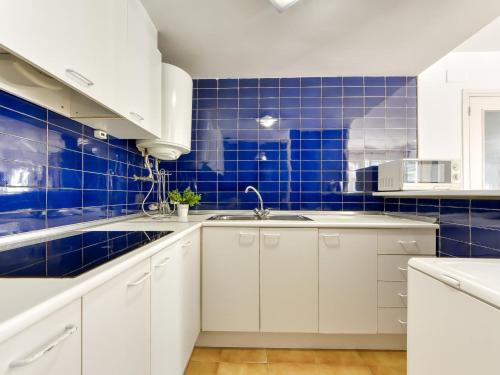 a kitchen with white cabinets and blue tiles at Apartment Platja de Roses-10 by Interhome in Roses