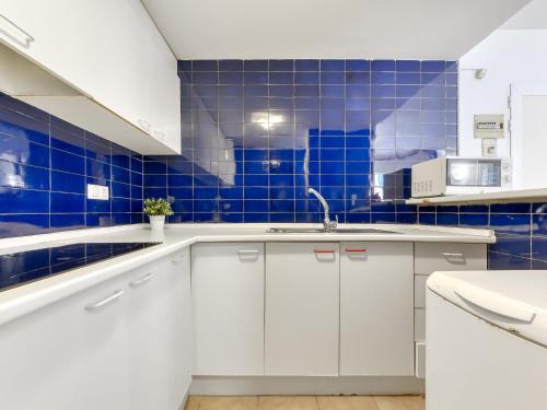 a kitchen with white cabinets and blue tiles at Apartment Platja de Roses-11 by Interhome in Roses