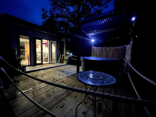 a wooden deck at night with a table and lights at Back to Nature Squirrels Lodge 1 bedroom lodge in South Molton