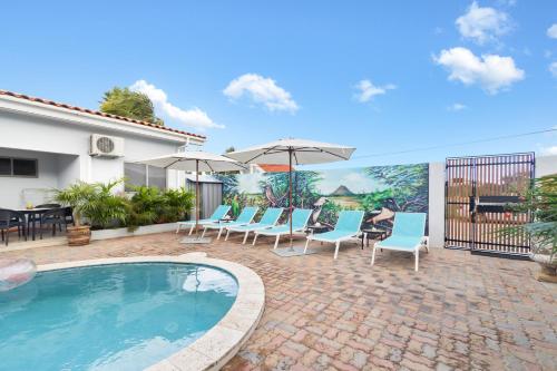 un patio con piscina, sillas y sombrillas en Little Paradise, en Noord