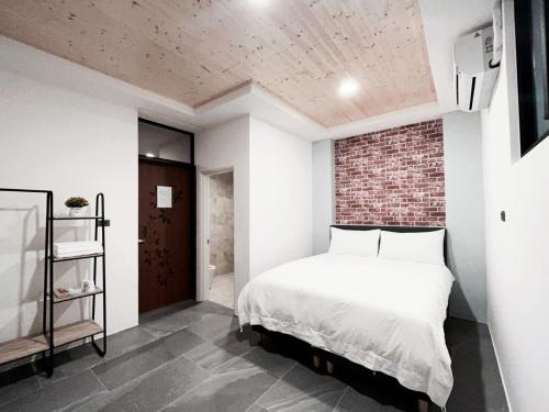 a bedroom with a white bed and a brick wall at Xianqing Yizhi Homestay in Taitung City