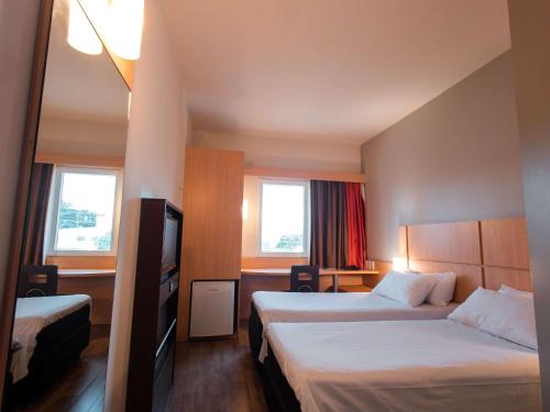 a hotel room with two beds and a television at ibis Presidente Prudente Manoel Goulart in Presidente Prudente