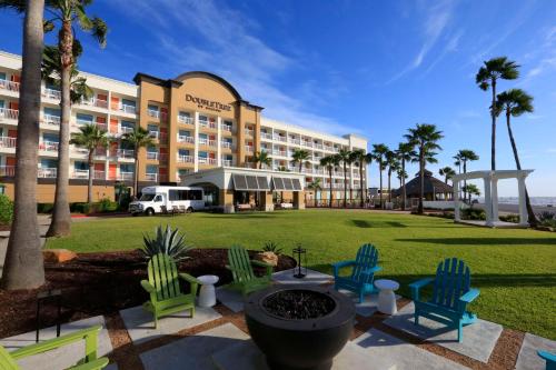 a hotel with a lawn and chairs and palm trees at DoubleTree by Hilton Galveston Beach in Galveston