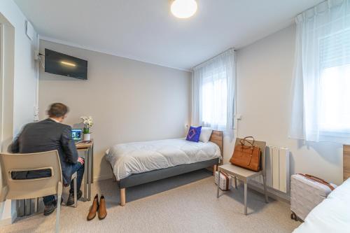 a man is sitting at a desk in a bedroom at Montempô Apparthôtel Lyon Viviani in Vénissieux