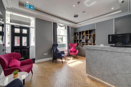 una sala de estar con sillas rosas y un bar en Mornington Hotel London Victoria, en Londres