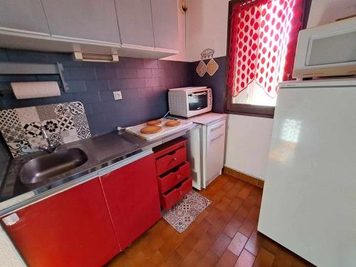 une petite cuisine avec des placards rouges et un four micro-ondes dans l'établissement Studio cabine mezzanine cosy avec terrasse, 6 couchages, parking privé - Marseillan - FR-1-326-521, à Le Castellas