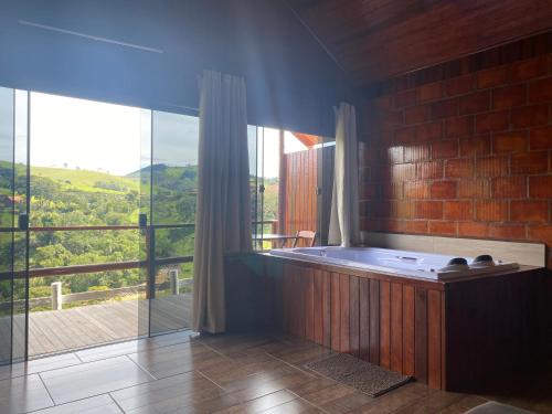 uma casa de banho com uma banheira e uma grande janela de vidro. em Chalés Canto Das Águas em Bueno Brandão