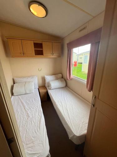 two beds in a small room with a window at B8, Three bedroom caravan - California Cliffs, Parkdean Resort, Scratby - Sleeps 8, bed linen, towels plus Wi-Fi included - Pet Friendly - Onsite entertainment and close to the beach! in Scratby