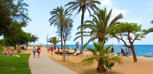 eine Gruppe von Menschen, die an einem Strand mit Palmen entlang spazieren in der Unterkunft Apart. Pineda de Mar-Sea and mountains views in Pineda de Mar