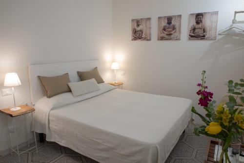 een wit bed in een kamer met 2 lampen en bloemen bij Guest house Le due lagune in Orbetello