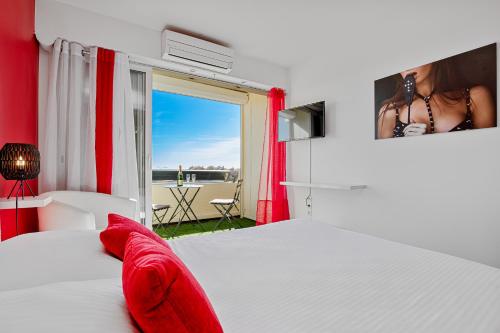 Cette chambre comprend un lit blanc avec des oreillers rouges et une fenêtre. dans l'établissement RED Port Nature, au Cap d'Agde