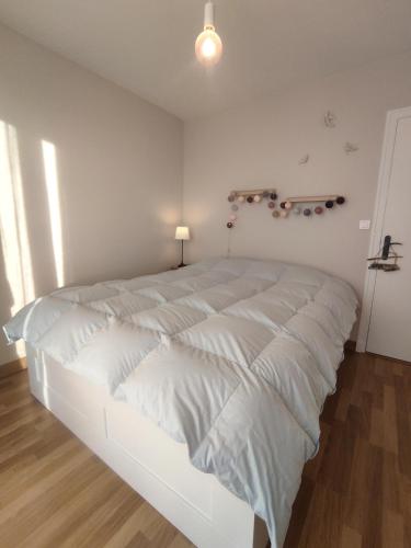Cette chambre blanche comprend un grand lit blanc et une lampe. dans l'établissement Idéal en amoureux, vue mer et jardin ! Appartement lumineux à Tharon-Plage, à Saint-Michel-Chef-Chef