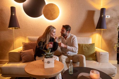 a man and woman sitting on a couch drinking wine at Hotel Nordik Adults Only - Over 14 in Andalo
