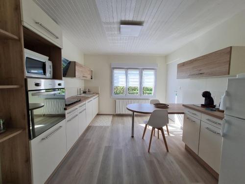 une cuisine avec des armoires blanches et une table à l'intérieur dans l'établissement Gîte familial au bord de la Meuse, proche Verdun, activités nature, confort tout inclus - FR-1-585-83, à Vilosnes-sur-Meuse