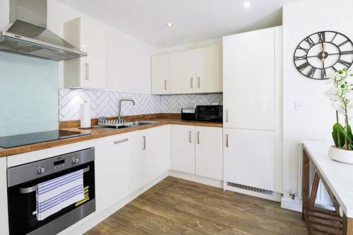 a kitchen with white cabinets and a clock on the wall at Exquisite Apartment with Balcony, Free Parking, Fast WiFi, and Smart TV by Yoko Property in Milton Keynes