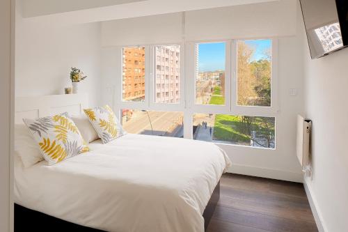 ein weißes Bett in einem Zimmer mit einem großen Fenster in der Unterkunft Playa de San Lorenzo in Gijón