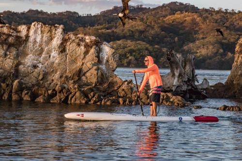 a man standing on a paddle board in the water at OPacifico Hotel Boutique in Playa Naranjo