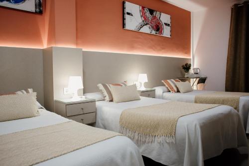 três camas num quarto com paredes cor de laranja em Pensión Mastil 16 em Málaga
