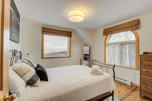 a bedroom with a white bed and two windows at Cozy Haven with Spa & Stunning Views in Baie-Saint-Paul