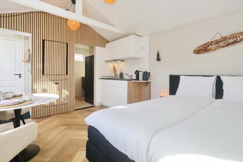 a bedroom with a large white bed and a kitchen at Huisje bij Zee 59 gratis parkeren in Noordwijk aan Zee