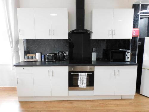 cocina con armarios blancos y encimera negra en Comfortable 4 bed Apt in Paisley Next to Station, en Paisley