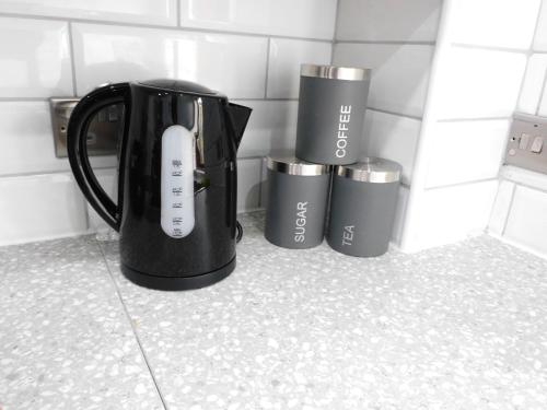 a black coffee pot on a counter with three cups at Charming 2 bed apt close to City and SEC Hydro in Glasgow