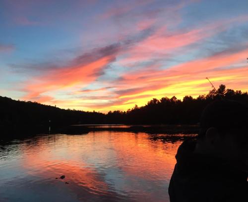 a person is looking at a sunset over a lake at Winter Lakefront Chalet - Serendipity Hideaway - Ski, Skate, Snowshoes & Relax by the Cozy Fire in Chertsey
