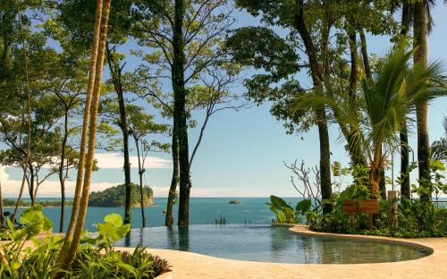 a pool in the middle of a beach with trees at Arenas Del Mar Beachfront & Rainforest Resort Member of the Cayuga Collection in Manuel Antonio